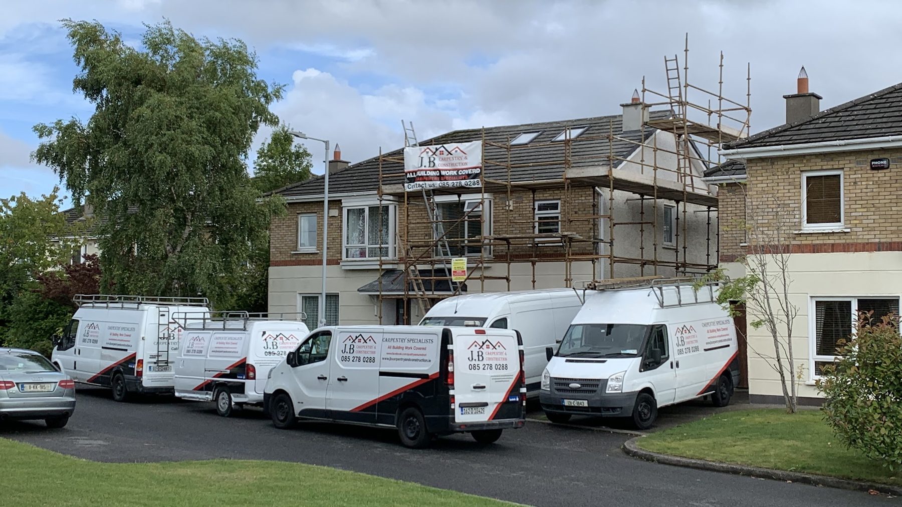 Four J.B Carpentry & Construction vans parked outside a house under scaffolding
