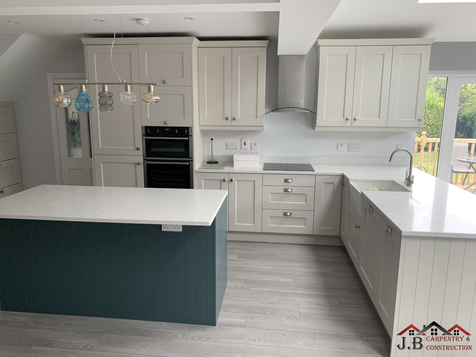 A shaker-style kitchen with a teal island and white stone worktops