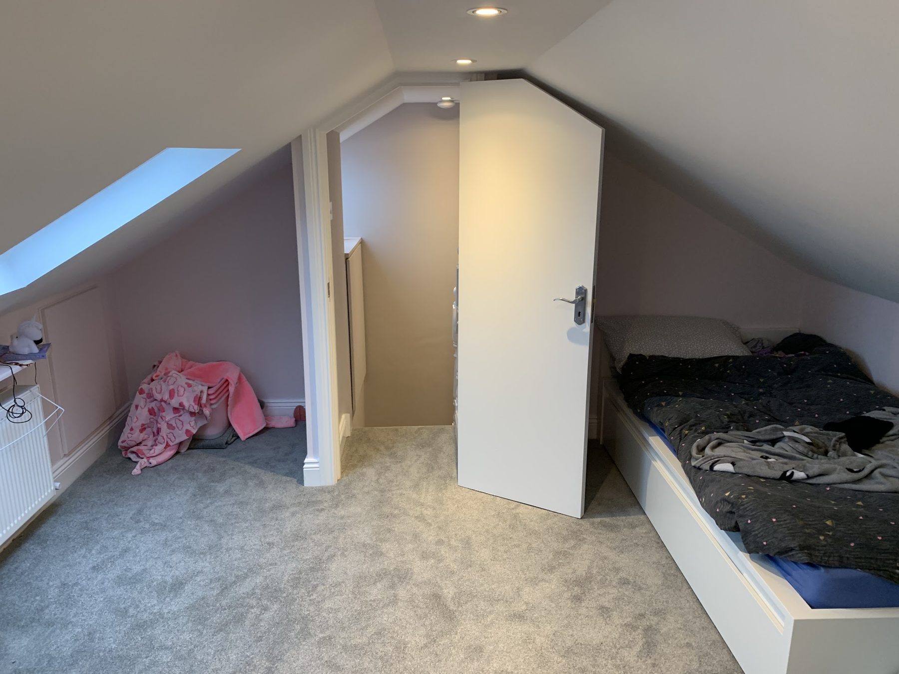 An attic bedroom with a roof window and a door set into the sloped ceiling