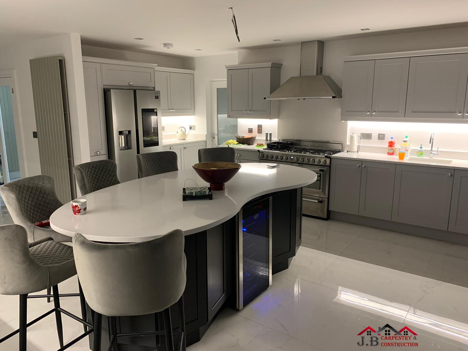 A kitchen with a curved island, grey bar stools and grey units