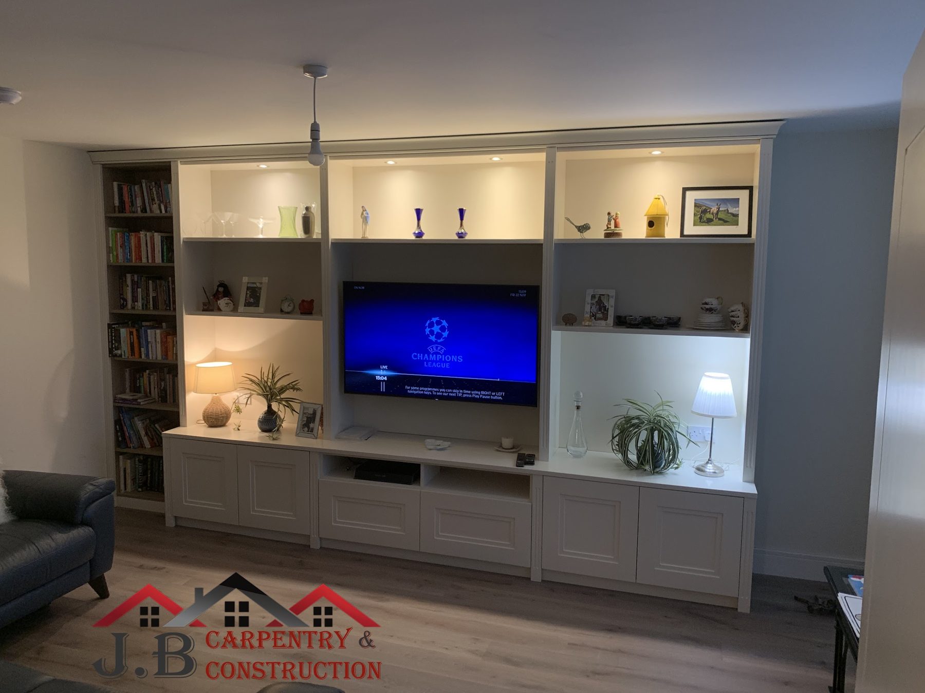 A built-in media wall with lit shelves above white cupboards